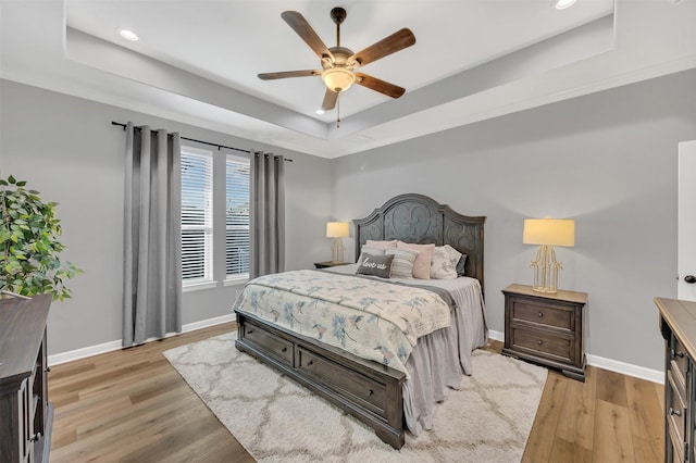 bedroom featuring a tray ceiling, recessed lighting, light wood finished floors, baseboards, and ceiling fan