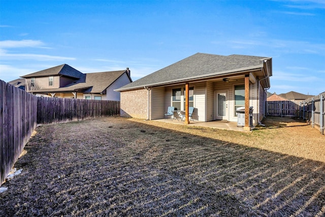 rear view of house with a lawn, roof with shingles, a fenced backyard, and a patio area