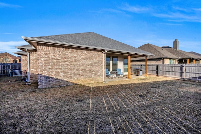 rear view of house featuring a patio area, brick siding, a fenced backyard, and roof with shingles