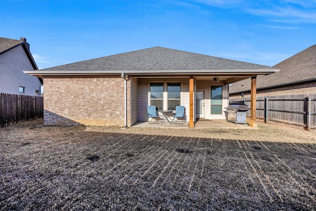 rear view of property with a patio, brick siding, a fenced backyard, and a shingled roof