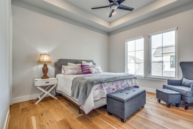 bedroom featuring a tray ceiling, baseboards, light wood-style floors, and ceiling fan