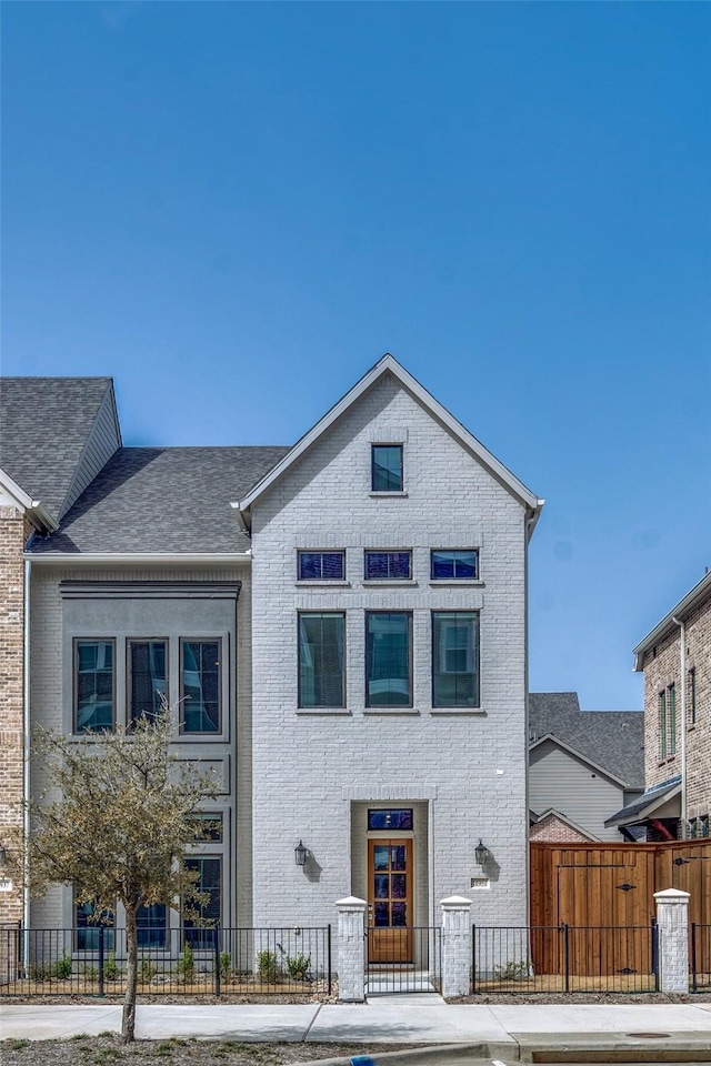 view of front of house with brick siding, a fenced front yard, and roof with shingles