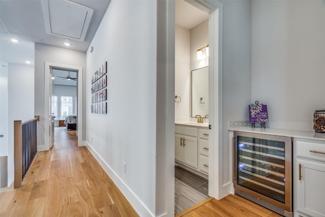 hallway with baseboards, attic access, a sink, wine cooler, and light wood-type flooring