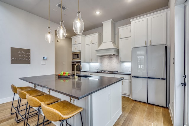 kitchen featuring dark countertops, custom range hood, appliances with stainless steel finishes, and a sink