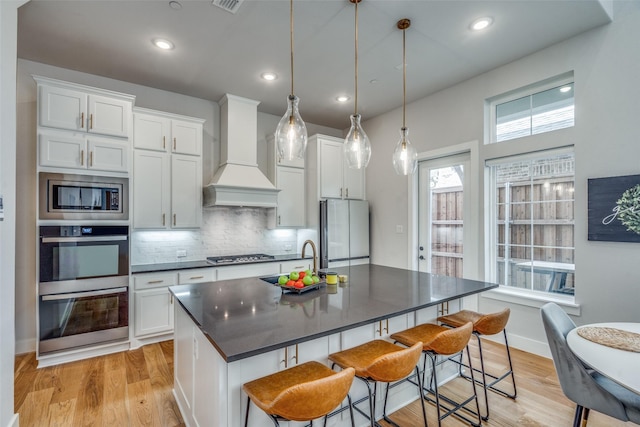 kitchen featuring decorative backsplash, custom range hood, appliances with stainless steel finishes, a kitchen bar, and dark countertops