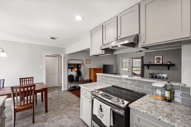 kitchen featuring visible vents, backsplash, under cabinet range hood, light stone counters, and stainless steel range with electric stovetop