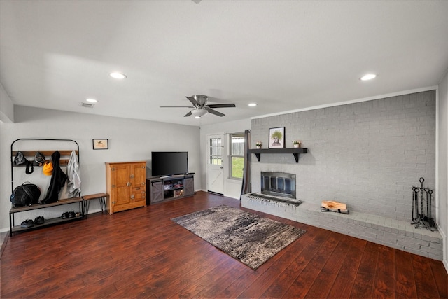 living room featuring visible vents, hardwood / wood-style flooring, brick wall, a brick fireplace, and ceiling fan