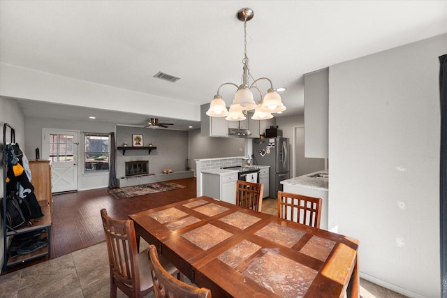 dining room with ceiling fan with notable chandelier, a fireplace, visible vents, and baseboards