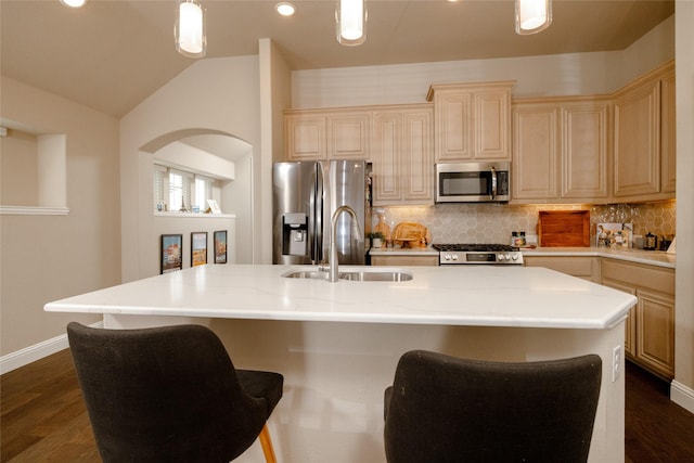 kitchen with dark wood finished floors, lofted ceiling, a kitchen island with sink, a sink, and appliances with stainless steel finishes