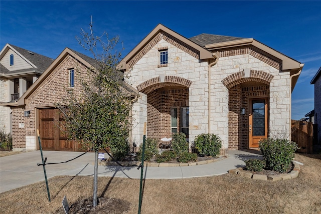 french country home with brick siding, stone siding, an attached garage, and concrete driveway