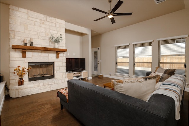 living room featuring visible vents, a ceiling fan, dark wood-style floors, a stone fireplace, and baseboards