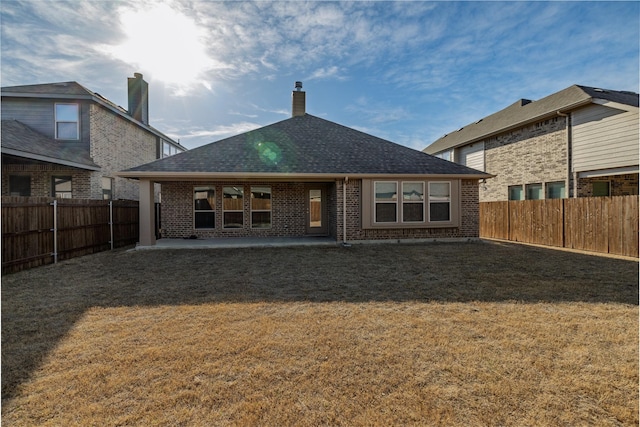 rear view of house with brick siding, roof with shingles, a yard, a fenced backyard, and a patio area