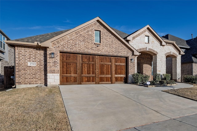 french country style house with driveway, a garage, brick siding, and stone siding