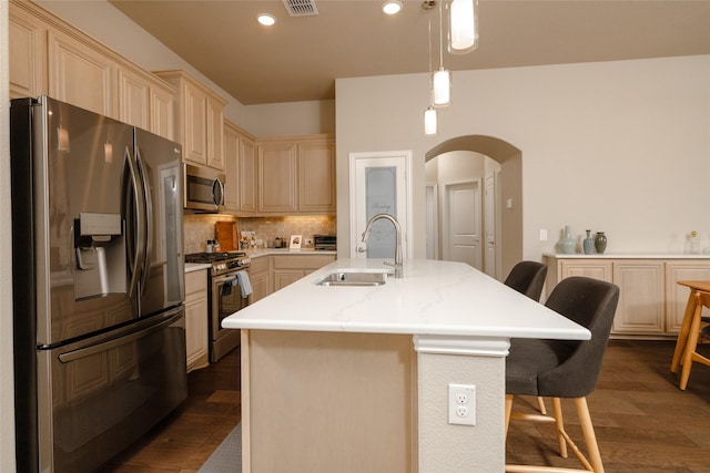 kitchen with a kitchen bar, a sink, tasteful backsplash, arched walkways, and appliances with stainless steel finishes