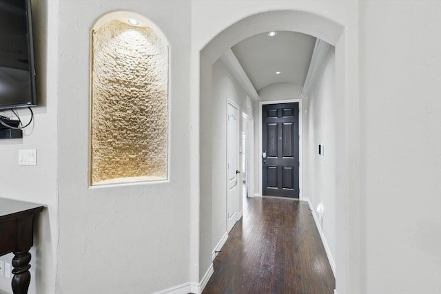 hall featuring wood finished floors, baseboards, and arched walkways