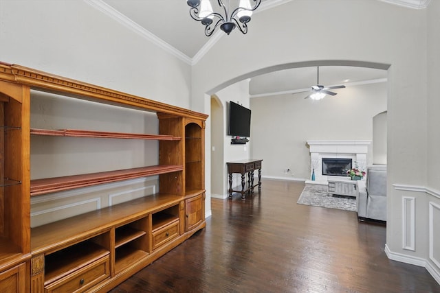 living room with dark wood-style floors, a glass covered fireplace, ceiling fan with notable chandelier, and crown molding