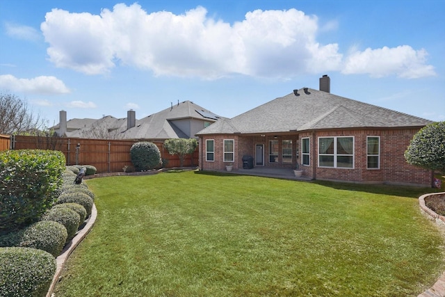 rear view of property with brick siding, a yard, a fenced backyard, and roof with shingles