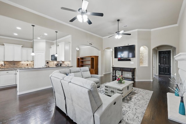 living room with arched walkways, dark wood finished floors, crown molding, and baseboards