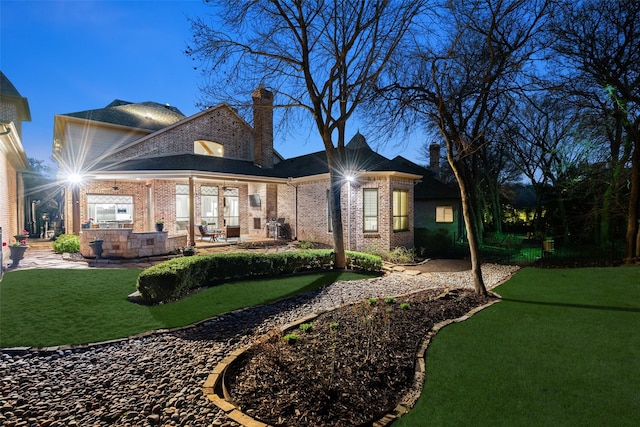 rear view of house featuring a patio area, a yard, a chimney, and brick siding