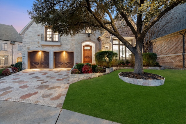 french country home with stone siding, driveway, an attached garage, and a front yard