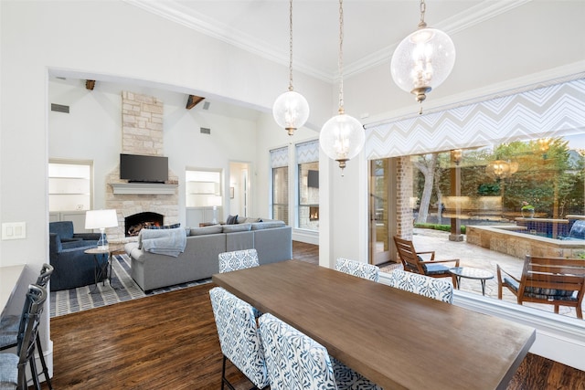 dining space with wood finished floors, crown molding, a fireplace, and a high ceiling