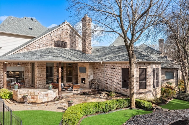 rear view of house with a patio, fence, a shingled roof, brick siding, and a chimney