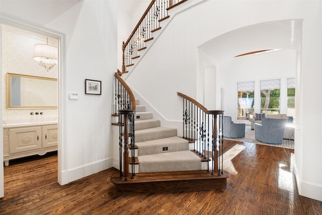 staircase featuring baseboards, arched walkways, wood finished floors, and a towering ceiling