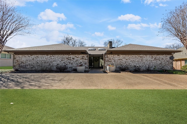 rear view of property featuring a shingled roof, a yard, brick siding, and a chimney