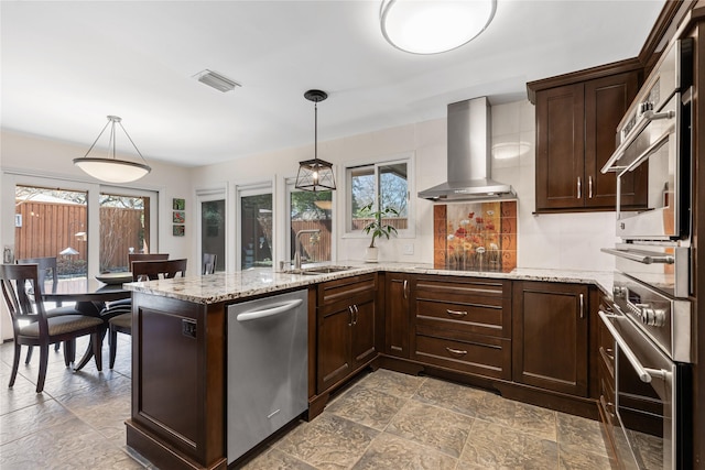 kitchen featuring a sink, visible vents, dark brown cabinetry, and wall chimney exhaust hood