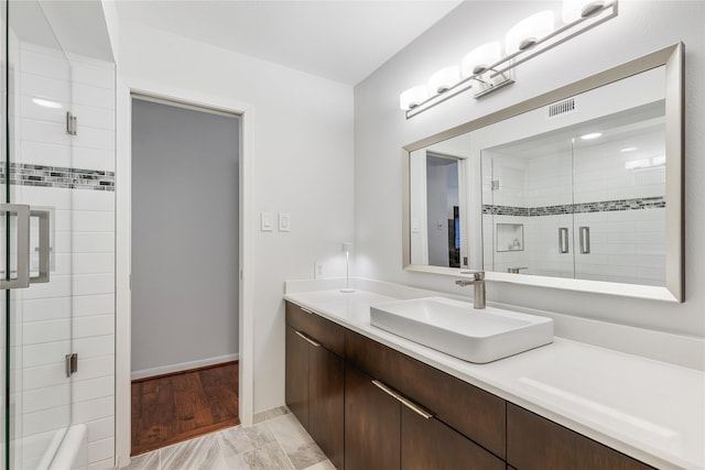 full bath with visible vents, tiled shower, vanity, and baseboards