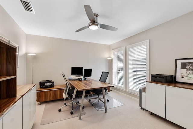 office space with visible vents, light colored carpet, baseboards, and a ceiling fan