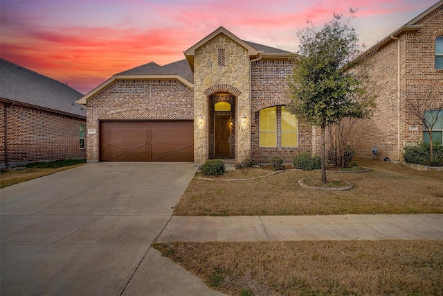 view of front of home featuring brick siding, a front lawn, a garage, stone siding, and driveway