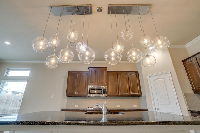 kitchen featuring decorative backsplash, dark stone counters, stainless steel microwave, and ornamental molding