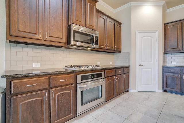 kitchen with stainless steel appliances, dark stone countertops, backsplash, ornamental molding, and light tile patterned floors