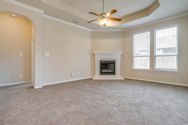 unfurnished living room with a ceiling fan, arched walkways, a tray ceiling, carpet flooring, and visible vents