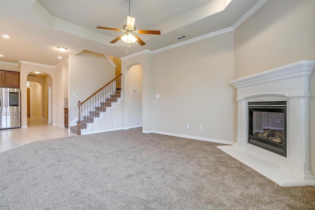 unfurnished living room featuring visible vents, light carpet, a glass covered fireplace, arched walkways, and a raised ceiling