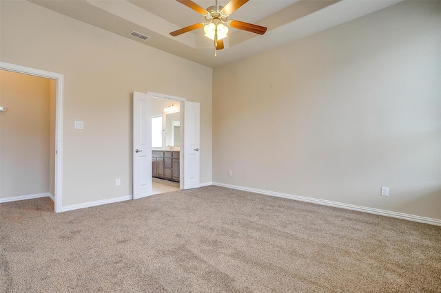 unfurnished bedroom with light carpet, ensuite bathroom, baseboards, visible vents, and a high ceiling