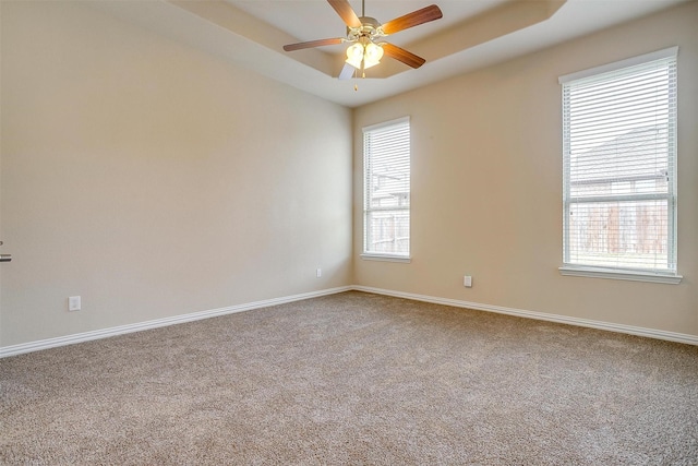 unfurnished room with ceiling fan, baseboards, a tray ceiling, and carpet