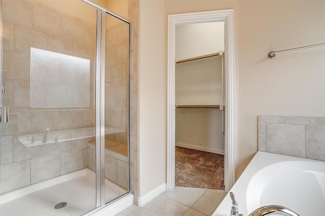bathroom featuring a walk in closet, a bath, tile patterned floors, and a stall shower