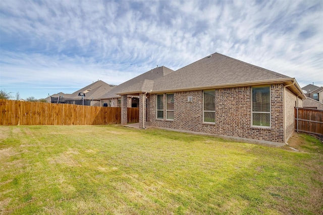rear view of house featuring brick siding, a yard, a shingled roof, and a fenced backyard
