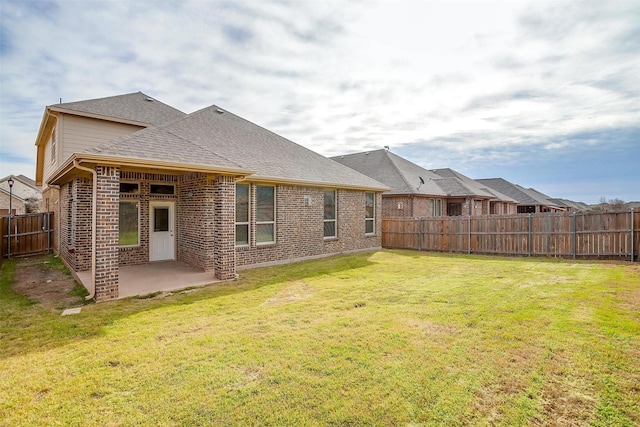 back of property featuring a lawn, a fenced backyard, roof with shingles, brick siding, and a patio area