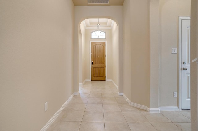 hall with visible vents, baseboards, ornamental molding, light tile patterned floors, and arched walkways