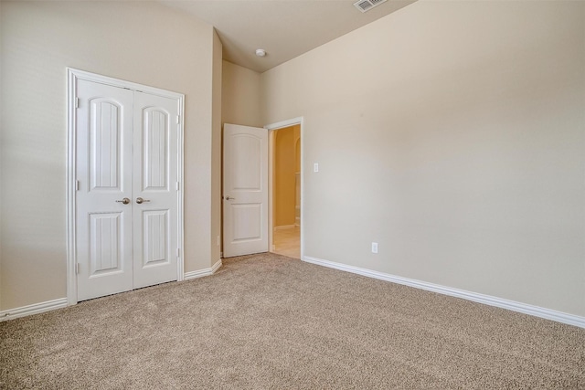 unfurnished bedroom with a closet, carpet floors, baseboards, lofted ceiling, and visible vents