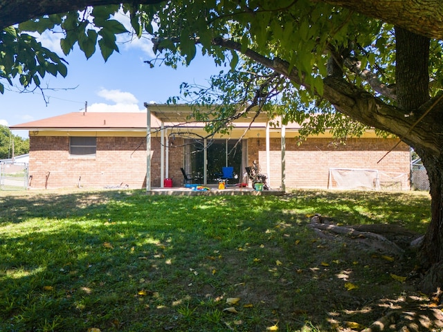 rear view of house with brick siding, a lawn, and a patio area