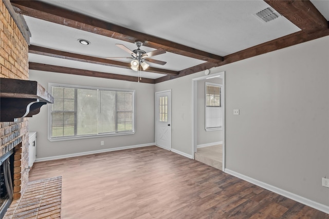 unfurnished living room with visible vents, beamed ceiling, wood finished floors, baseboards, and a brick fireplace