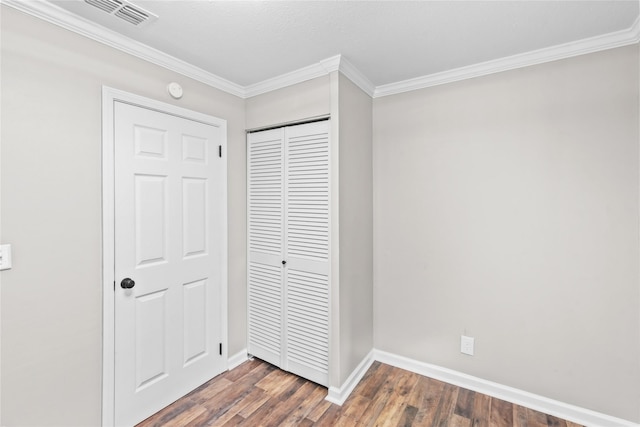 unfurnished bedroom featuring visible vents, dark wood-type flooring, a closet, crown molding, and baseboards