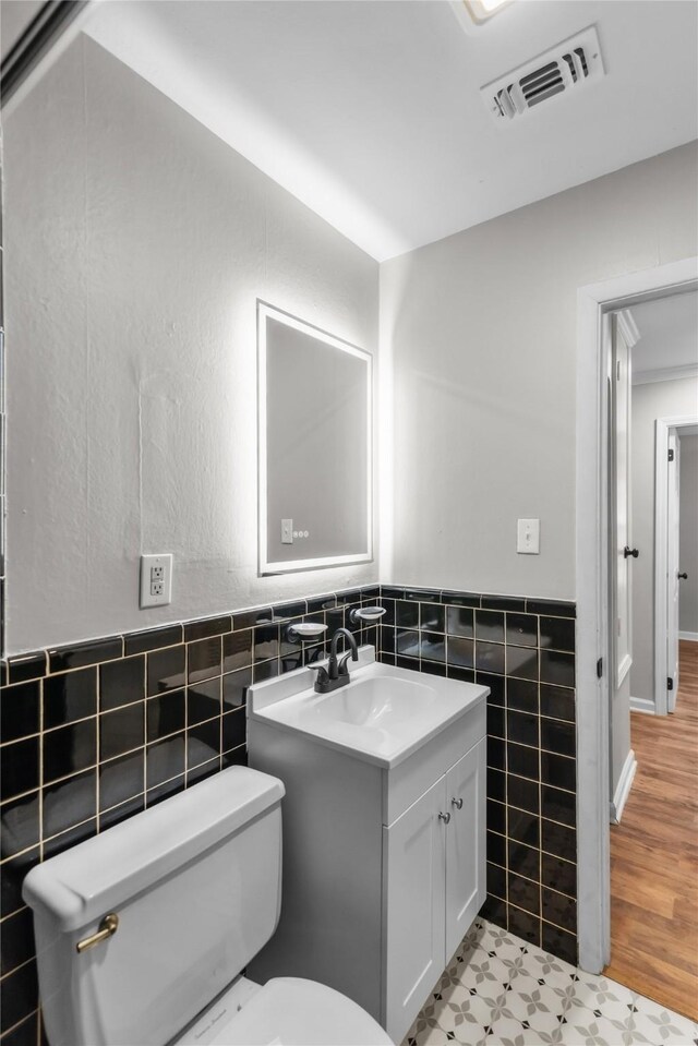 bathroom featuring visible vents, a wainscoted wall, toilet, vanity, and tile walls