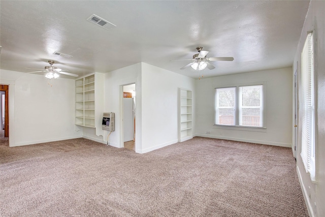 unfurnished living room with visible vents, built in shelves, heating unit, carpet flooring, and baseboards