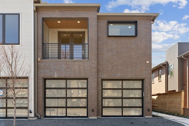 contemporary house featuring a balcony, an attached garage, and brick siding