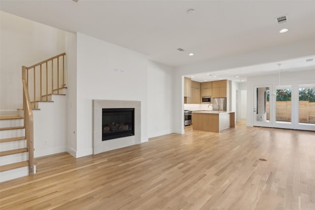 unfurnished living room featuring a glass covered fireplace, stairs, recessed lighting, and light wood-type flooring